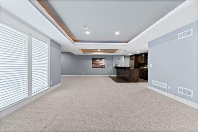 unfurnished living room featuring ornamental molding, light colored carpet, and a tray ceiling