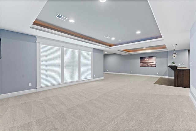 unfurnished living room featuring light carpet, sink, and a raised ceiling