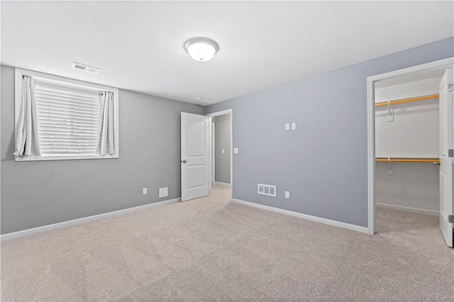 unfurnished bedroom with a walk in closet, light colored carpet, and a closet