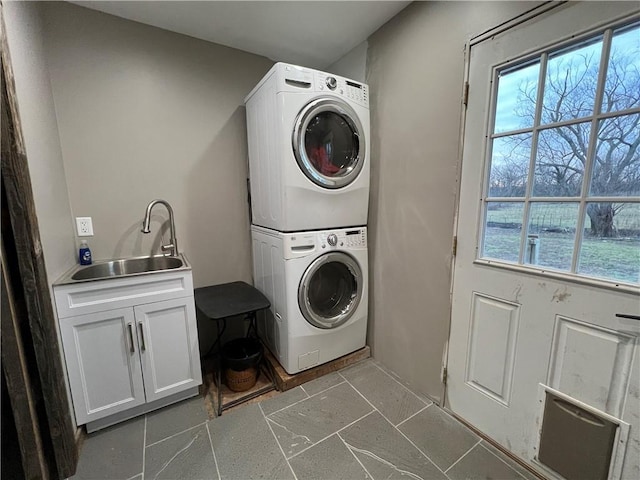 washroom featuring stacked washer / dryer, a healthy amount of sunlight, sink, and cabinets