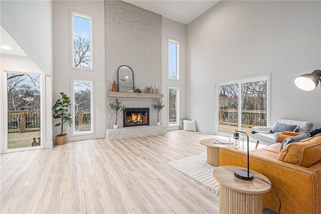 living room featuring a large fireplace, light wood-type flooring, and a towering ceiling