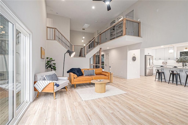 living room with ceiling fan, light hardwood / wood-style flooring, and a towering ceiling