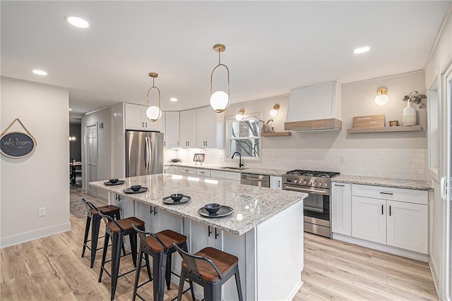 kitchen with appliances with stainless steel finishes, premium range hood, sink, pendant lighting, and white cabinetry