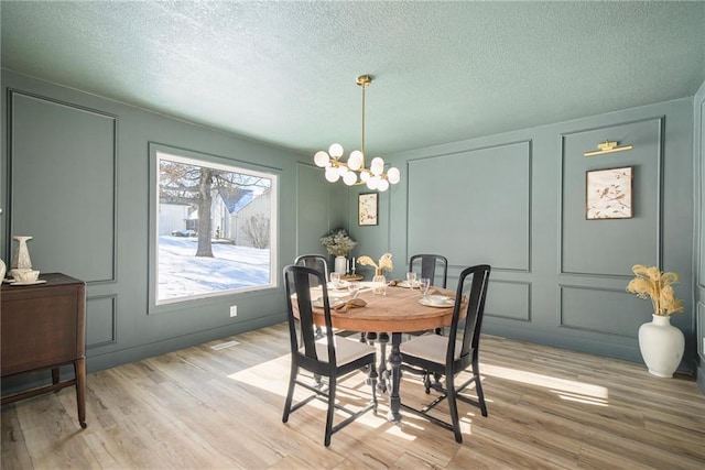 dining room featuring light wood-type flooring, a textured ceiling, and an inviting chandelier