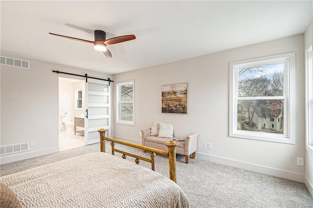 carpeted bedroom featuring multiple windows, a barn door, ensuite bath, and ceiling fan