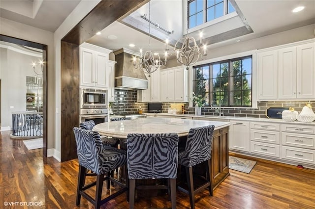 kitchen with premium range hood, a kitchen island, a breakfast bar, appliances with stainless steel finishes, and white cabinetry