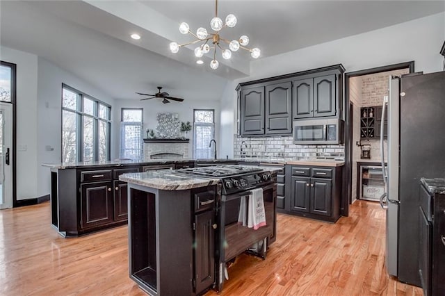 kitchen featuring kitchen peninsula, ceiling fan with notable chandelier, stainless steel appliances, decorative light fixtures, and a kitchen island