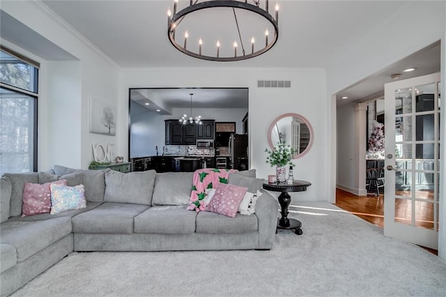 carpeted living room featuring crown molding, french doors, and a chandelier