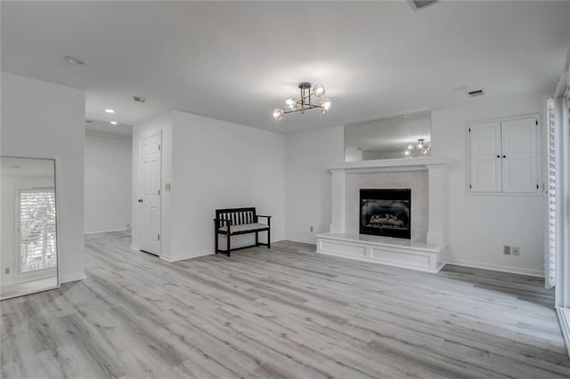 unfurnished living room featuring light hardwood / wood-style floors, an inviting chandelier, and a tiled fireplace