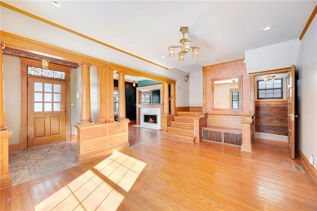 foyer featuring a warm lit fireplace, light wood finished floors, visible vents, radiator heating unit, and ornate columns