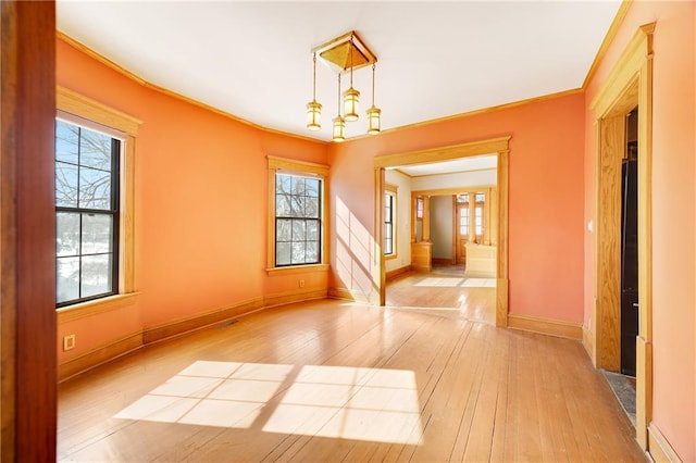 spare room with ornamental molding, light wood-style flooring, and baseboards