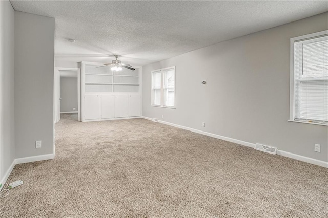 empty room with carpet, a textured ceiling, built in features, and ceiling fan