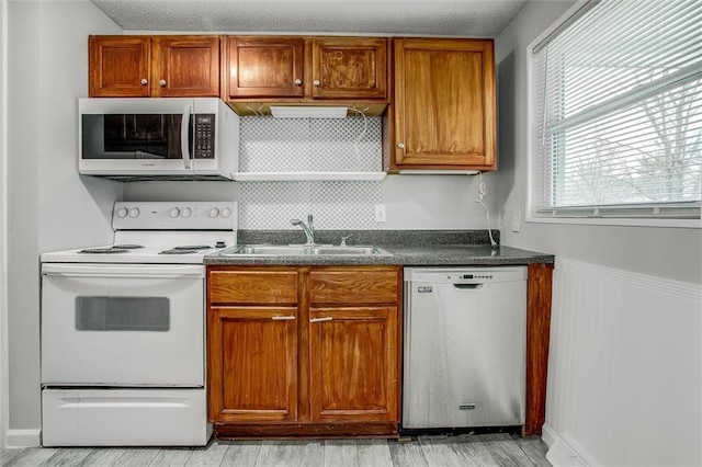 kitchen with a textured ceiling, white appliances, light hardwood / wood-style floors, and sink