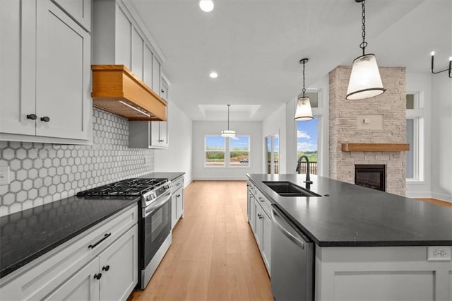 kitchen featuring appliances with stainless steel finishes, tasteful backsplash, a fireplace, a sink, and light wood-style flooring