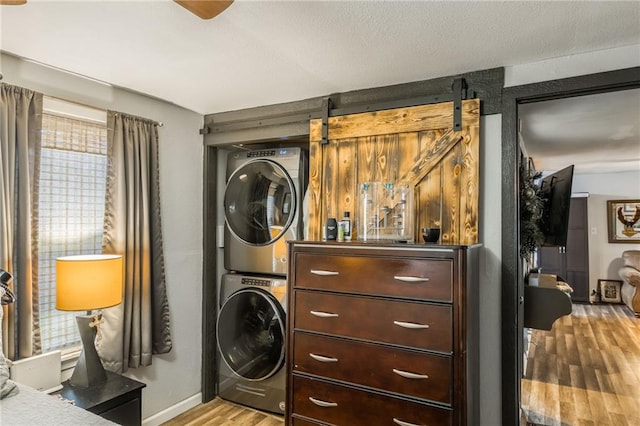 laundry room with light wood-type flooring, a barn door, and stacked washer and dryer