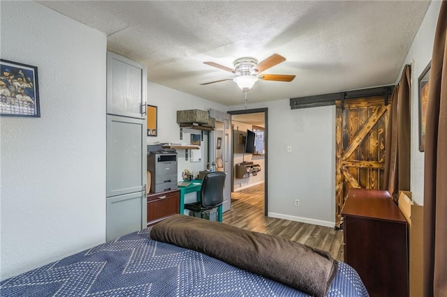 bedroom with a barn door, ceiling fan, wood-type flooring, and a textured ceiling