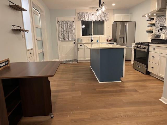 kitchen with white cabinets, a center island, wall chimney range hood, and appliances with stainless steel finishes