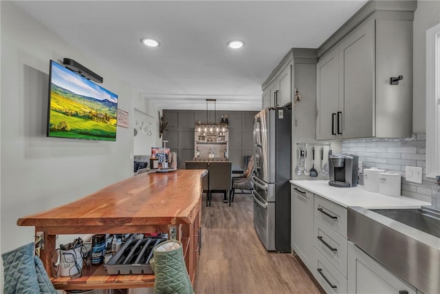 kitchen featuring pendant lighting, stainless steel refrigerator, tasteful backsplash, gray cabinetry, and light hardwood / wood-style flooring