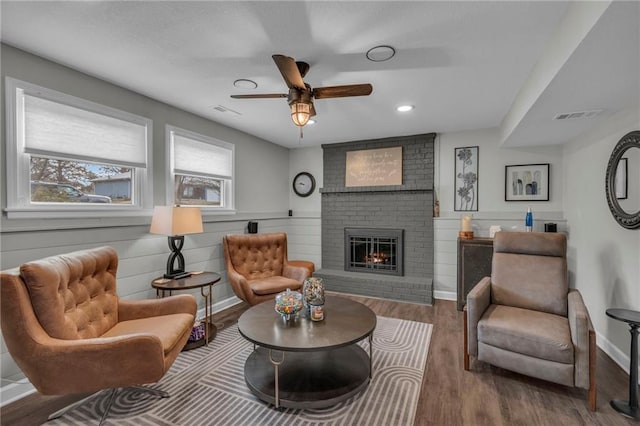 living area featuring ceiling fan, wood-type flooring, and a fireplace