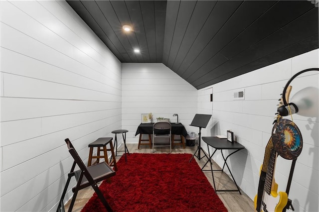 dining area with wooden walls, light hardwood / wood-style flooring, and vaulted ceiling