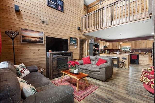 living room featuring a towering ceiling, light hardwood / wood-style floors, and wood walls