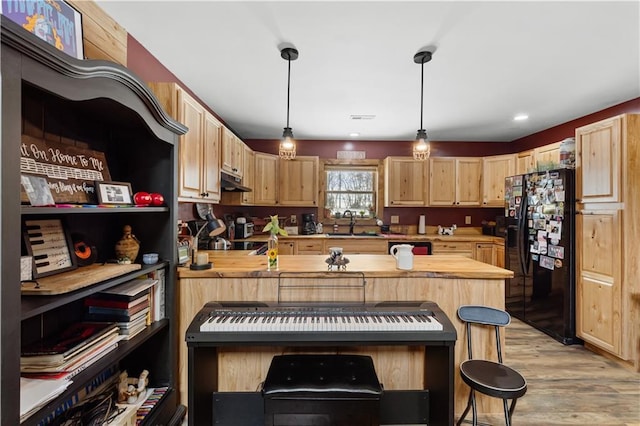 kitchen featuring butcher block countertops, black refrigerator with ice dispenser, light brown cabinets, and decorative light fixtures