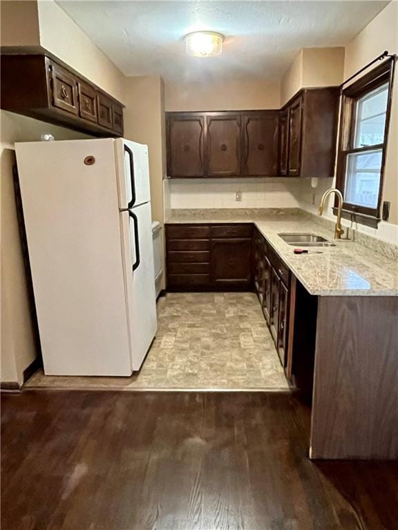 kitchen with light stone countertops, dark brown cabinetry, sink, light hardwood / wood-style flooring, and white fridge