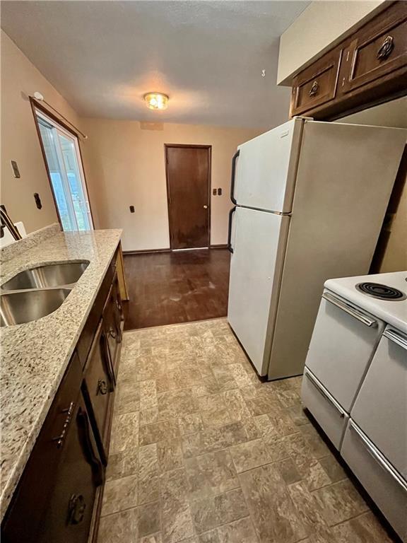 kitchen with white appliances, dark brown cabinetry, light stone countertops, and sink