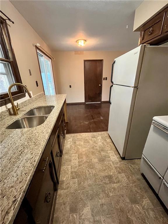 kitchen featuring dark brown cabinetry, sink, light stone counters, white refrigerator, and range