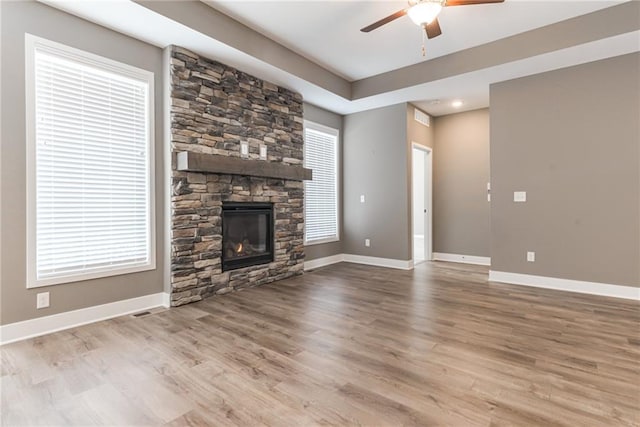 unfurnished living room featuring ceiling fan, baseboards, a stone fireplace, and wood finished floors