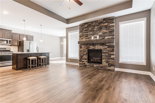 living room with light wood-type flooring, a ceiling fan, a tray ceiling, a fireplace, and baseboards