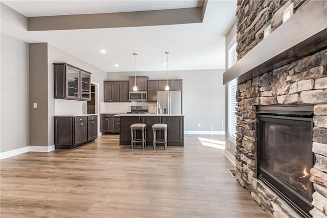 kitchen with light wood-type flooring, stainless steel appliances, a stone fireplace, light countertops, and dark brown cabinets