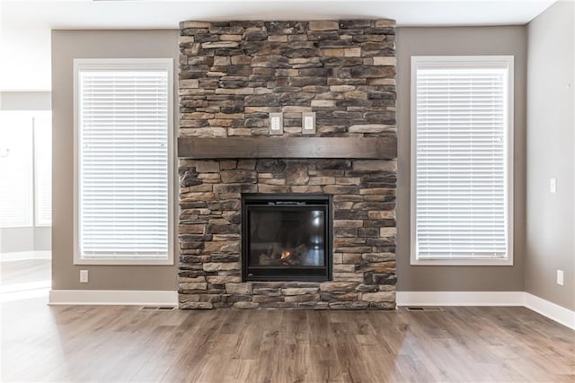 details featuring a stone fireplace, wood finished floors, visible vents, and baseboards