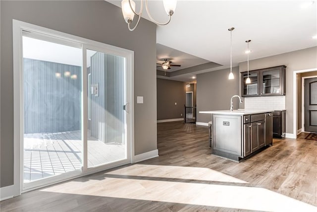 kitchen with light wood-style flooring, a center island with sink, decorative light fixtures, tasteful backsplash, and light countertops