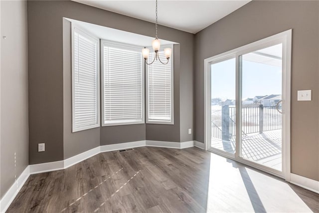 unfurnished dining area featuring baseboards, an inviting chandelier, and dark wood finished floors