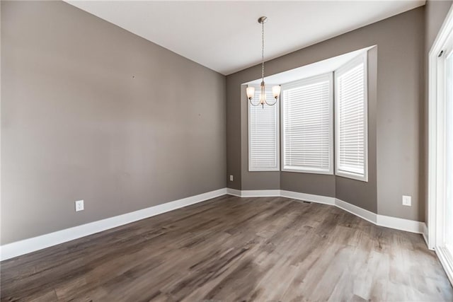 spare room with a notable chandelier, wood finished floors, and baseboards