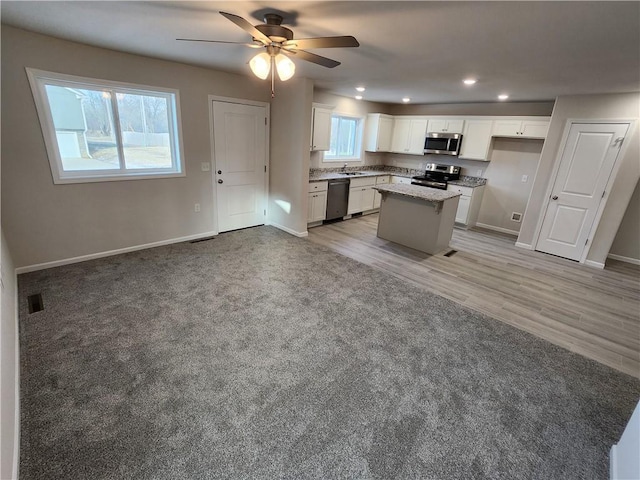 kitchen featuring ceiling fan, a healthy amount of sunlight, a kitchen island, white cabinets, and appliances with stainless steel finishes