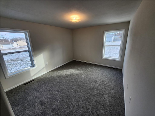 empty room with dark colored carpet and a wealth of natural light