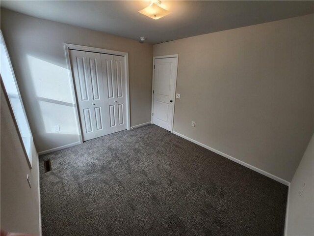 unfurnished bedroom with dark colored carpet and a closet