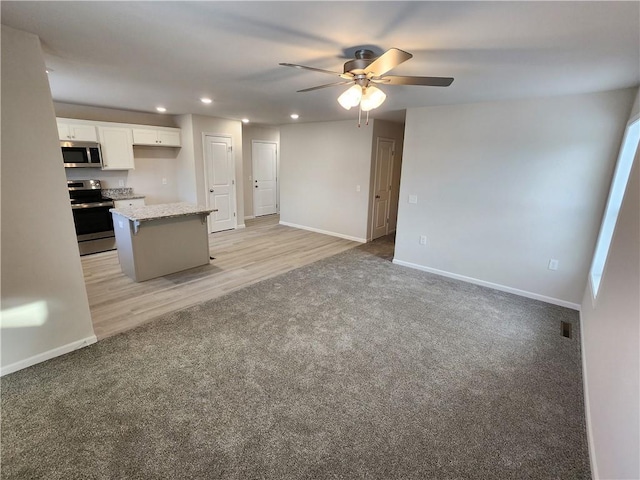 kitchen featuring light carpet, ceiling fan, appliances with stainless steel finishes, a kitchen island, and white cabinetry