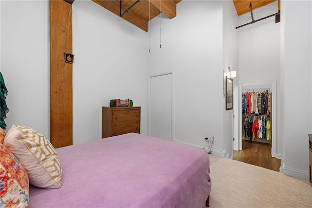 bedroom featuring wood ceiling, a towering ceiling, a spacious closet, a closet, and beam ceiling