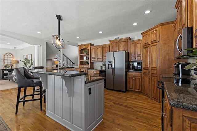 kitchen featuring decorative light fixtures, a kitchen bar, a kitchen island with sink, dark wood-type flooring, and appliances with stainless steel finishes