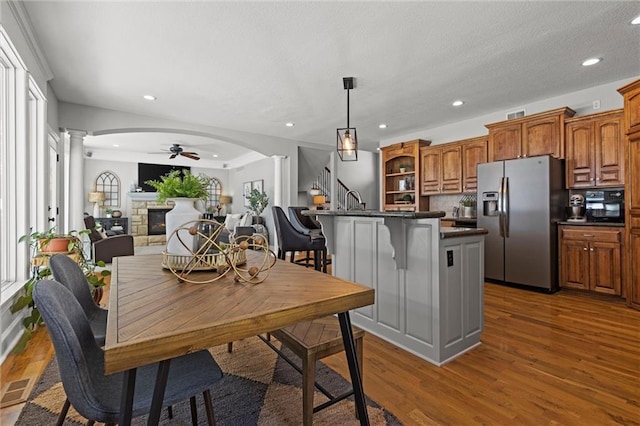 kitchen featuring stainless steel refrigerator with ice dispenser, dark hardwood / wood-style flooring, ceiling fan, decorative columns, and a breakfast bar