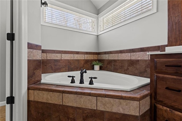 bathroom featuring tiled bath, vanity, and lofted ceiling