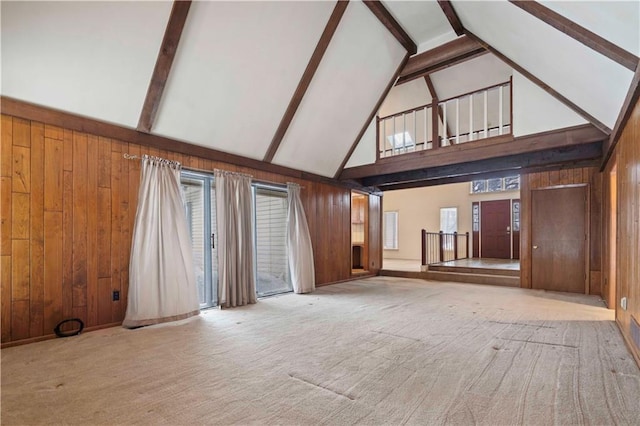 unfurnished living room featuring high vaulted ceiling, light colored carpet, beam ceiling, and wood walls