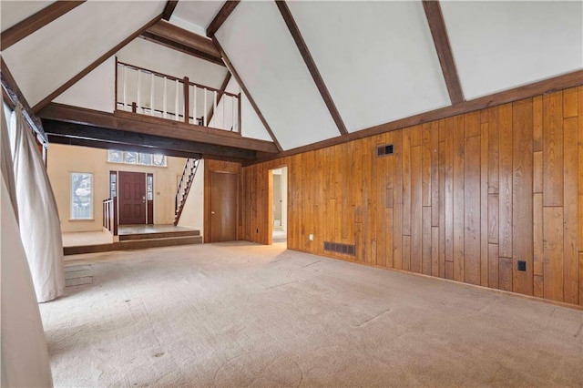 unfurnished living room featuring high vaulted ceiling, wood walls, carpet floors, and beamed ceiling