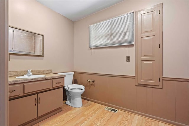 bathroom featuring hardwood / wood-style flooring, toilet, vanity, and wooden walls