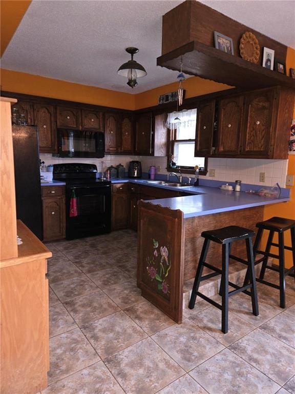 kitchen featuring kitchen peninsula, decorative backsplash, a breakfast bar, dark brown cabinetry, and black appliances