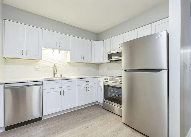 kitchen with backsplash, sink, light hardwood / wood-style flooring, appliances with stainless steel finishes, and white cabinetry