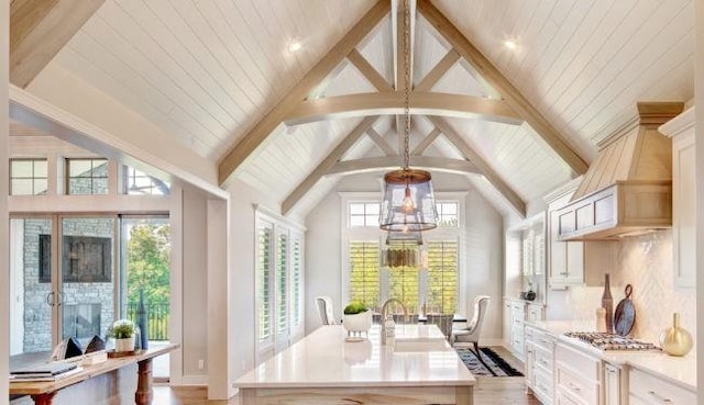 kitchen featuring a kitchen island with sink, beamed ceiling, pendant lighting, light hardwood / wood-style floors, and decorative backsplash